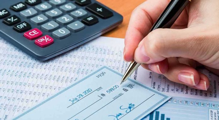 Hand writing a check beside a calculator and financial documents