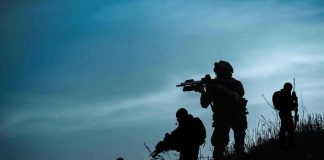 Silhouetted soldiers patrolling a hillside at dusk