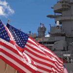 Trump Signed. Someone Was LOCKED OUT American flags in front of a naval ship under a blue sky