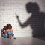 Child sitting against wall with shadow of an adult pointing