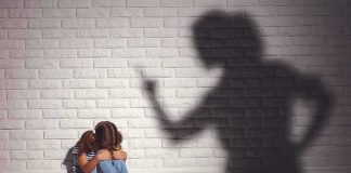 Child sitting against wall with shadow of an adult pointing