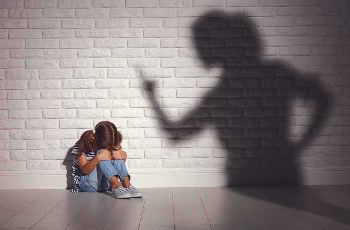 Child sitting against wall with shadow of an adult pointing