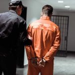 Accused Prayer DISRUPTER Caught By His CHEAP Trick Police officer escorting handcuffed inmate in orange jumpsuit