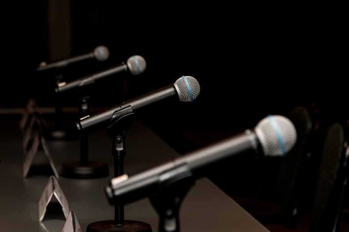 Row of microphones on stands at a panel table