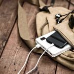 Beige backpack with phone charging on power bank and sunglasses