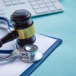 Gavel and stethoscope on medical clipboard near keyboard