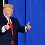 Donald Trump giving two thumbs up in front of a blue curtain