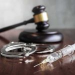 Syringe with handcuffs and judge's gavel on a wooden table