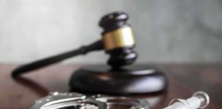 Syringe with handcuffs and judge's gavel on a wooden table