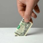 Hand inserting a folded dollar bill into a small slot