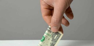 Hand inserting a folded dollar bill into a small slot