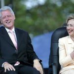 Bill Clinton and Hillary Clinton laughing and applauding while seated outdoors