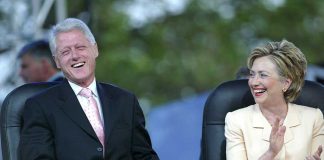 Bill Clinton and Hillary Clinton laughing and applauding while seated outdoors