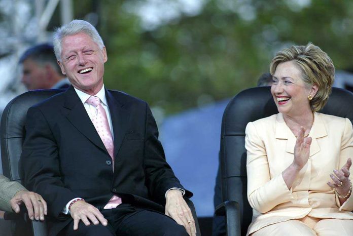 Bill Clinton and Hillary Clinton laughing and applauding while seated outdoors