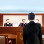 man in suit facing judges in a courtroom