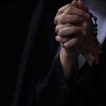 Hands clasped in prayer holding a rosary