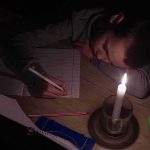 Child doing homework by candlelight at a desk