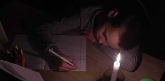 Child doing homework by candlelight at a desk