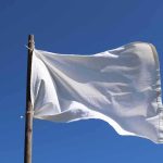 White flag on wooden pole against clear blue sky