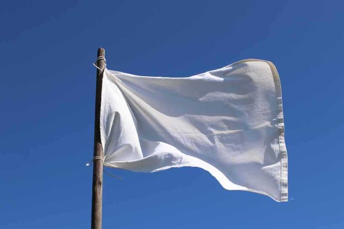 shutterstock_1976764391 White flag on wooden pole against clear blue sky