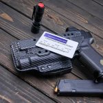 Handgun with holster, permit card, flashlight, and magazine on wooden surface
