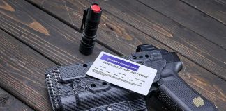 Handgun with holster, permit card, flashlight, and magazine on wooden surface