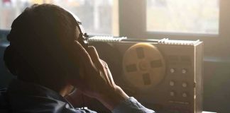 Person listening with headphones to a reel-to-reel tape recorder