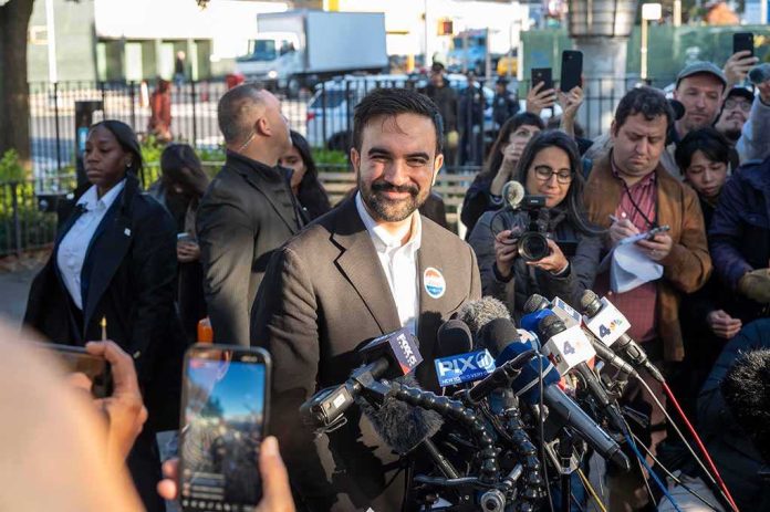 Zohran Mamdani speaks at a press conference; Julia Bacha is visible among the crowd