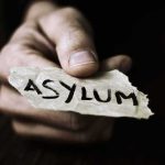 Judges Let Terror Camp Worker Seek Asylum — Wait Till You Read WHY Hand holding torn paper with the word asylum