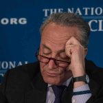 man with glasses resting forehead on hand at event podium