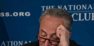 man with glasses resting forehead on hand at event podium
